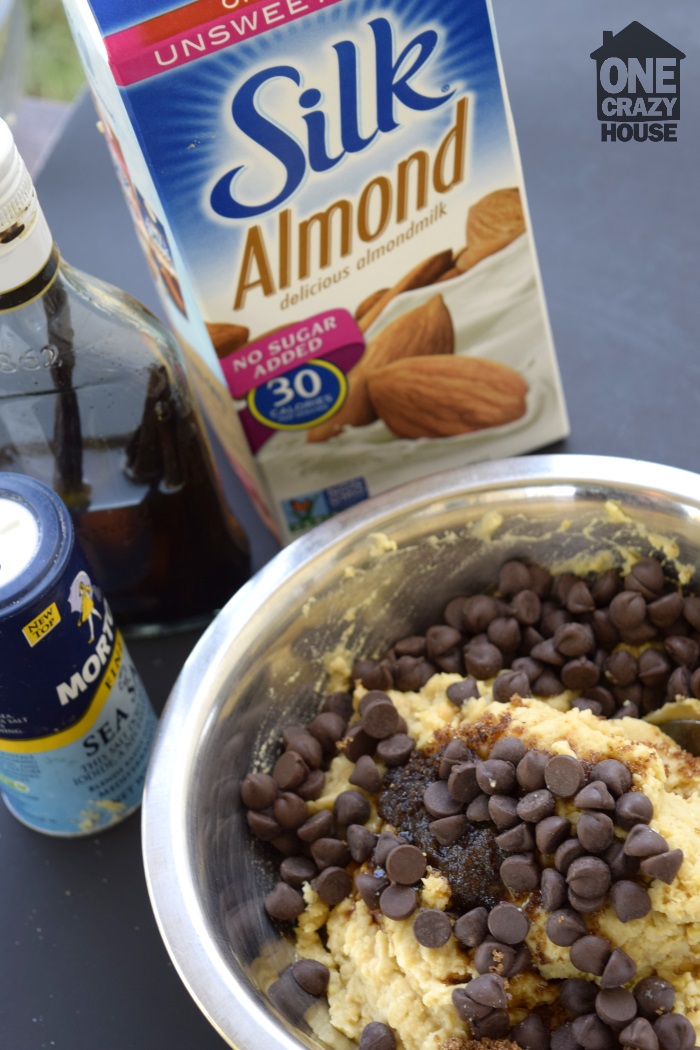 Chocolate Chip Cookie Dough Dip – With a Shocking Ingredient
- Garbanzo Chocolate Chip Cookie Dough ingredients being combined in a metal mixing bowl with containers of salt and almond milk in the background. 