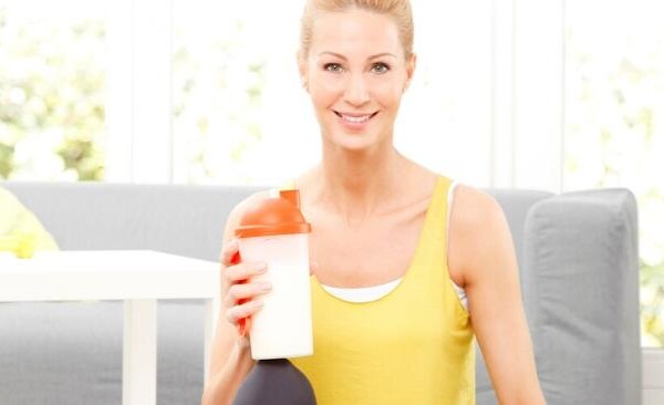 woman sitting on the floor with weights holding a protein shake