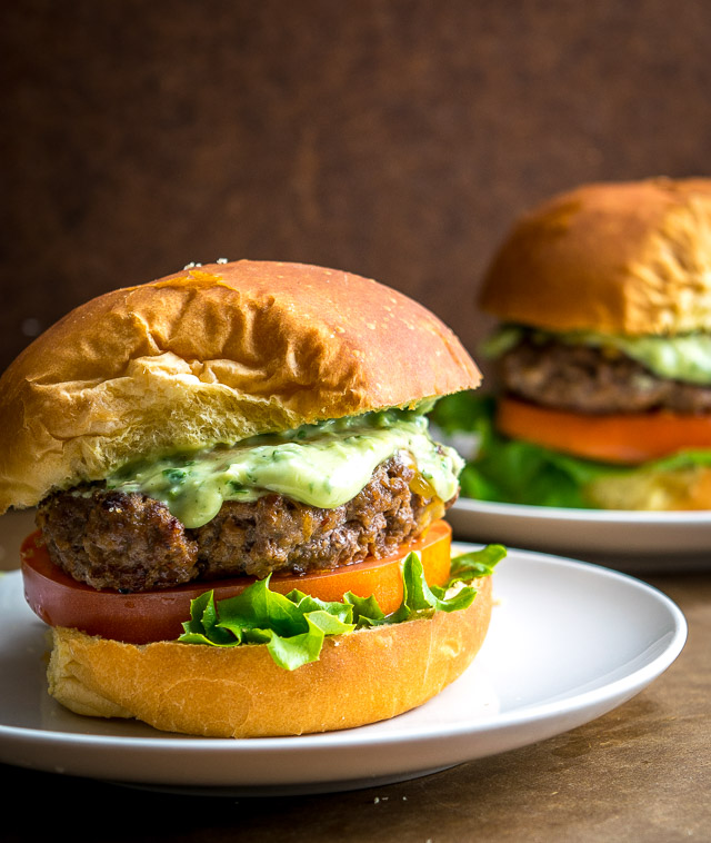 2 chipotle burgers on separate plates with creamy avocado sauce 