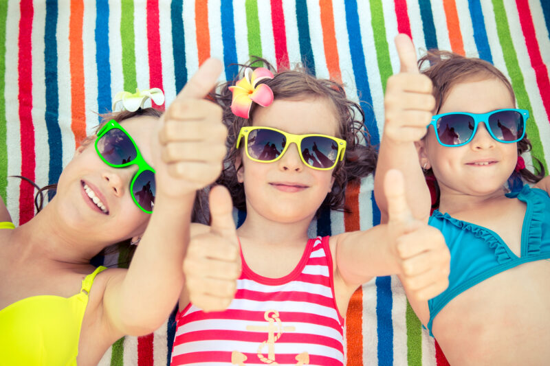 3 young girls in swimsuits with sunglasses laying on a beach towel on spring break