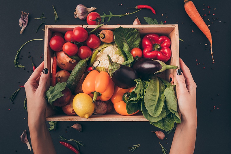 Woman holding a crate filled with foods for a plant based diets including vegetables, herbs and fruit.