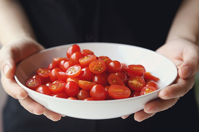 Close up of hands holding a white bowl filled with sliced cherry tomatoes.