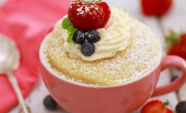 mug cake in a pink mug with cream and fruit on top