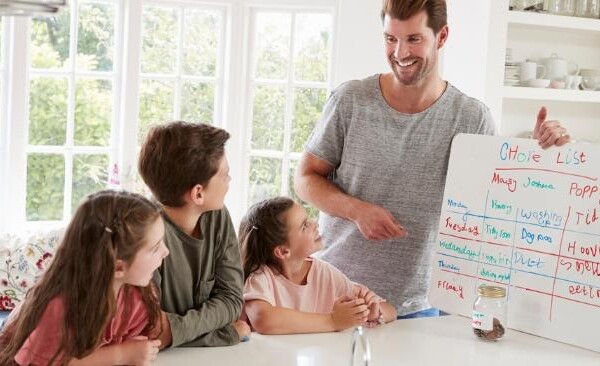 father with three kids going over a whiteboard chore chart