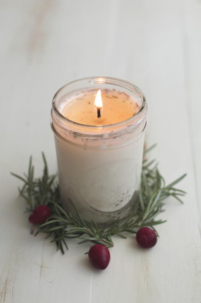 DIY candle with a lit flame and a wreath of greenery around the base of the jar