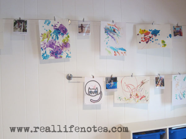 kids art displayed on a wall hanging from curtain rods