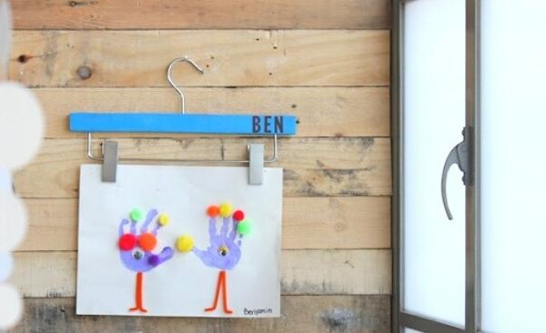 kids art hanging on a wall using a skirt hanger