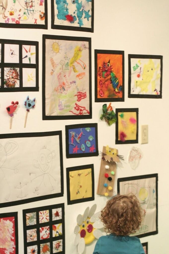 kids art displayed on a wall with tape as frame for each piece