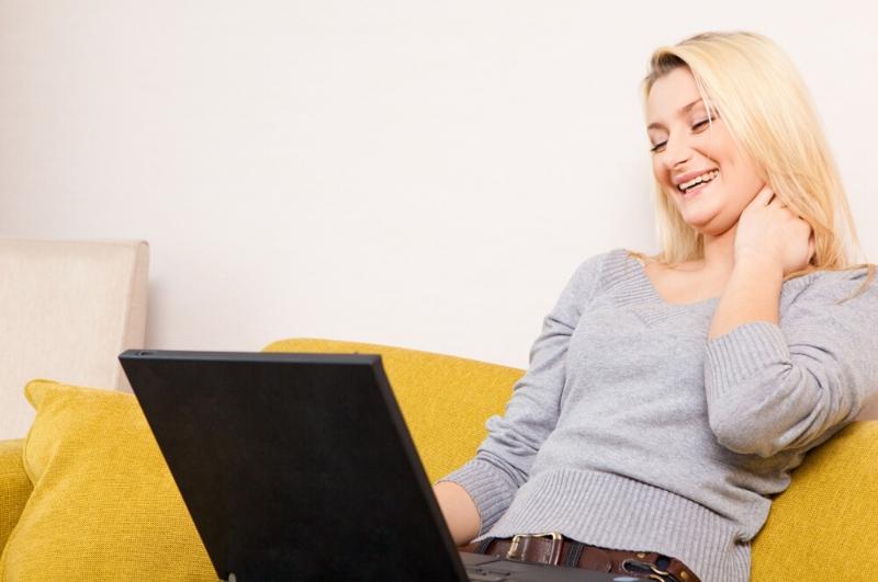 woman sitting on couch with her laptop laughing as a mood booster