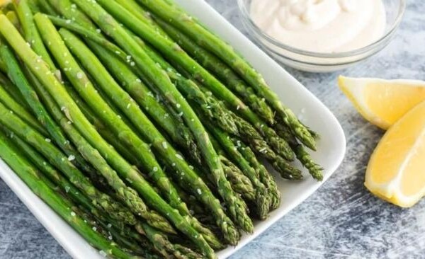 bowl of stalks of asparagus with lemon and a dish with dip