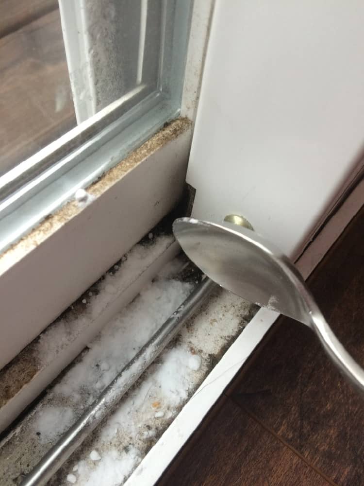 A spoon spilling baking soda on dirty window tracks before cleaning