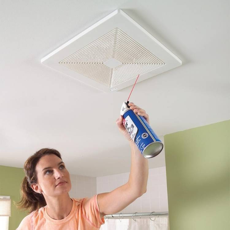 a woman cleaning her bathroom exhaust fan with a can of air