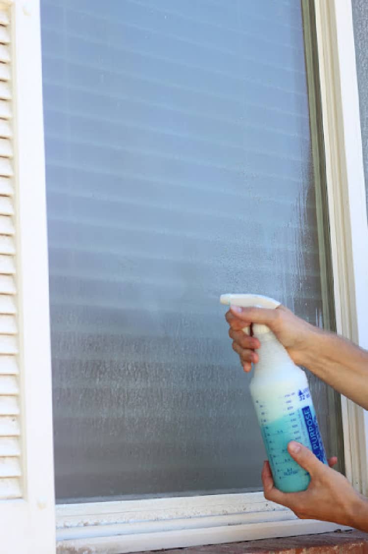 Person spraying windows with hard water stains with a diy window cleaning solution