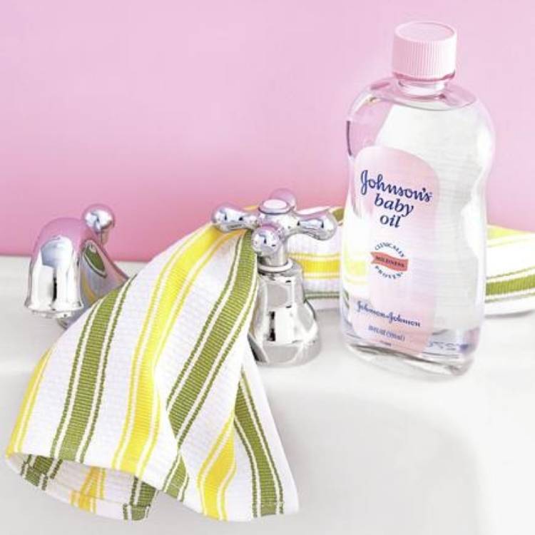 baby oil beside a sink tap with towel on top of the sink 