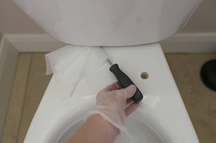 cleaning under the toilet tank with a wipe and a screwdriver