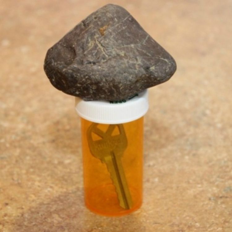 House key hidden inside pill bottle under rock