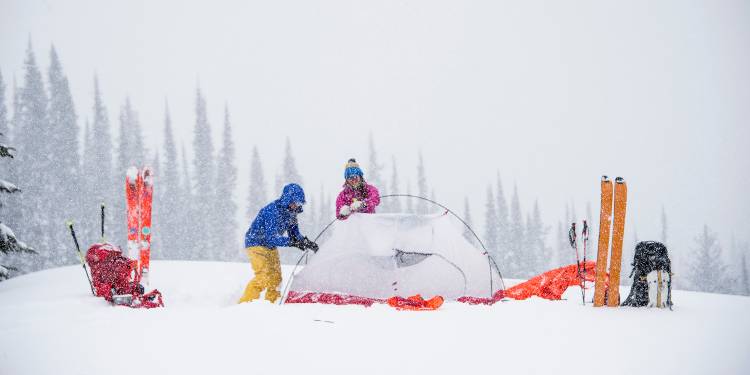 cold-weather-camping image of a campsite in the snow with two campers and their gear around a tent