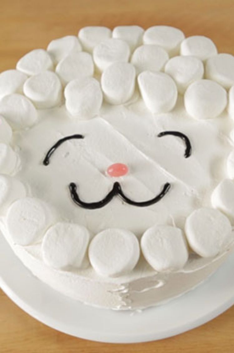 White frosted cake with large marshmallows along the sides and black icing for a smile and eyes