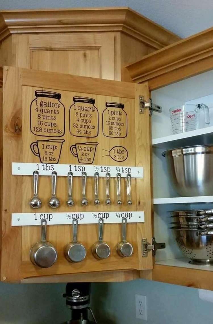 Open kitchen cabinet with measuring cup stickers with measurements on them, strip of wood with hooks with measuring cups hanging from them