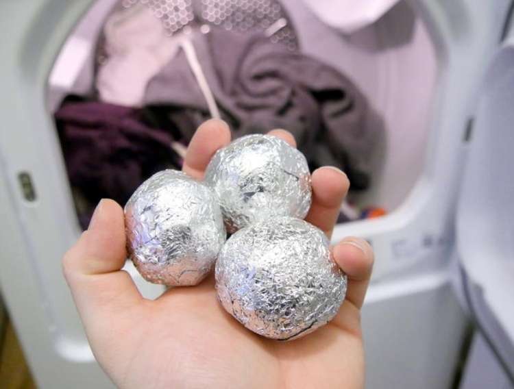 OneCrazyHouse Fastest way to dry clothes Hand holding 2 aluminum foil balls in front of an open dryer with clothes inside.