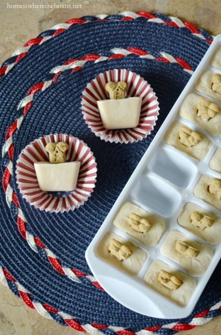 Frozen yogurt dog treats with bone shaped biscuits poking out in cupcake wrappers next to ice cube tray full of dog treats.