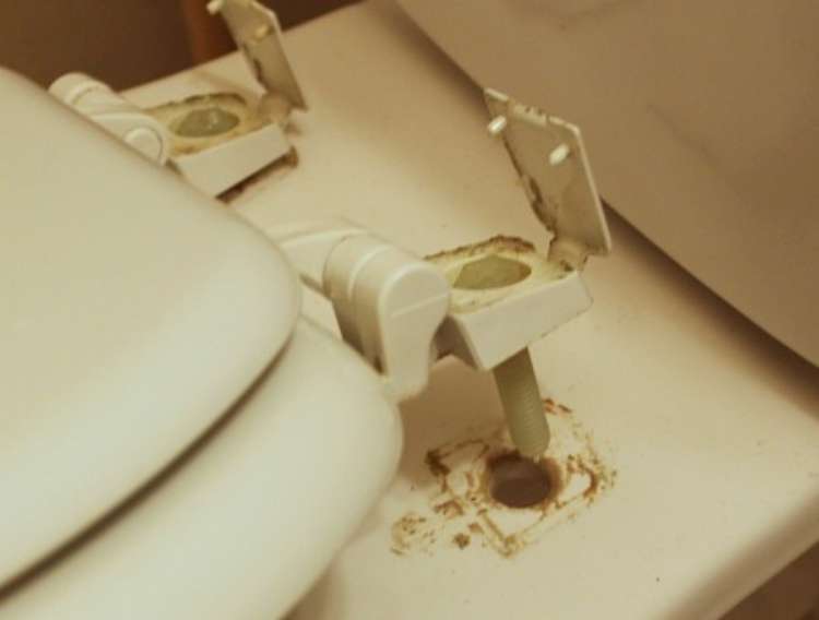 Toilet seat pulled up from the attachment to the bowl to show the grime that has accumulate there