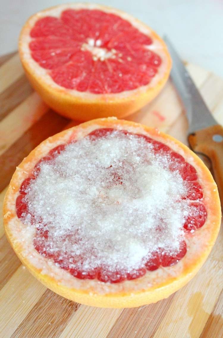 Two halves of a sliced grapefruit on a wooden cutting board. The half closest to the camera is covered in salt.