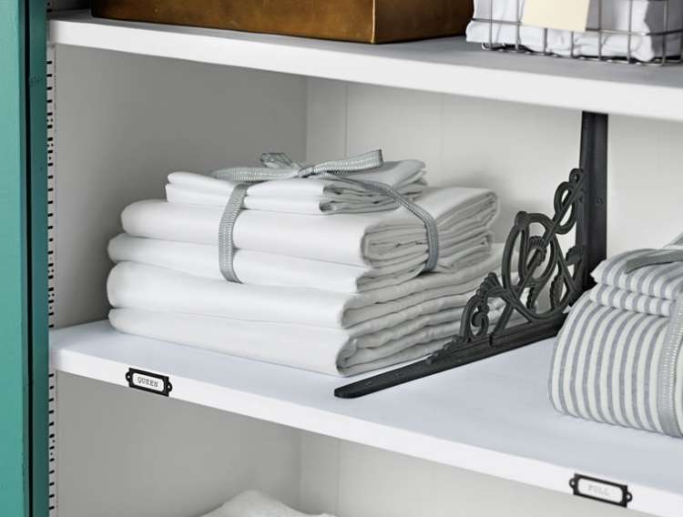 Towels folded and neatly stacked on a shelf with a label on the front of the shelf. Divider sectioning off area for towels, with another compartment with linens next to it. 