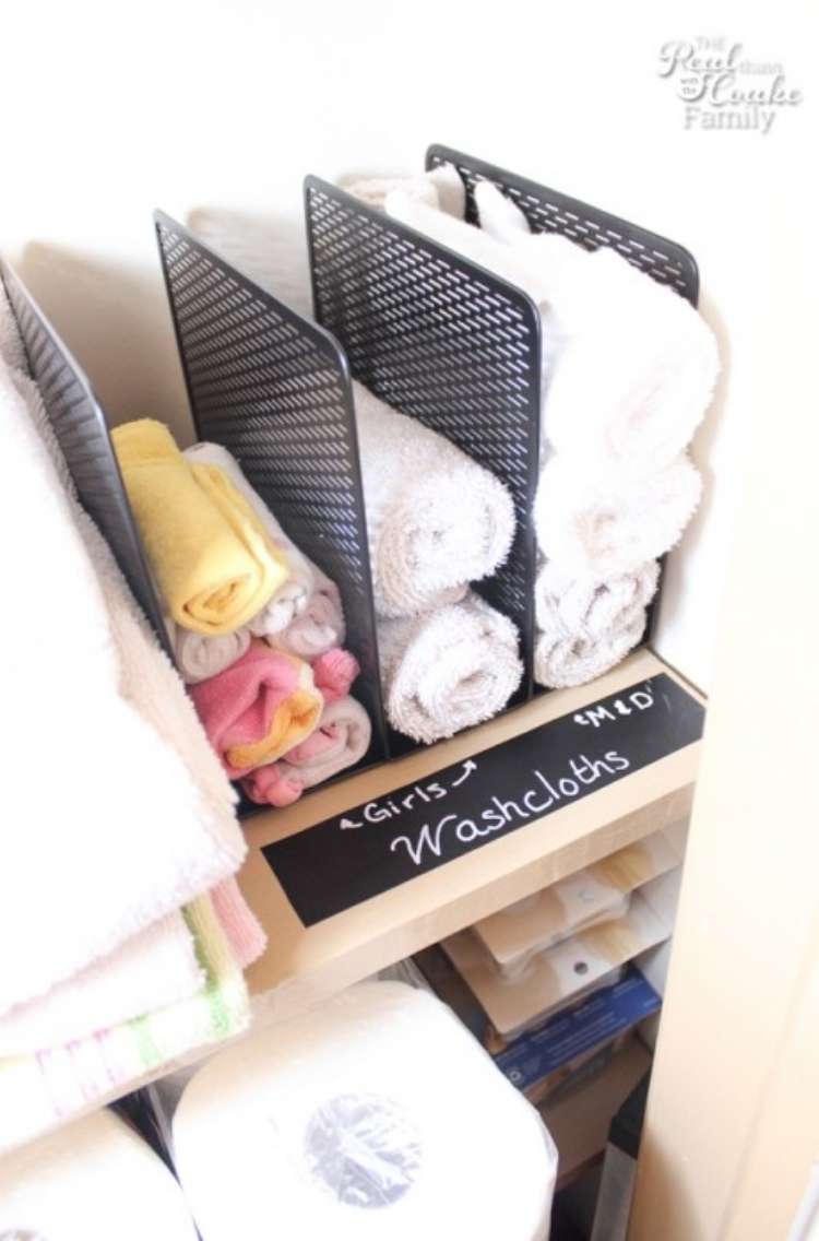 Shelves in linen closet with hand towels rolled and stacked in magazine holders on top shelf