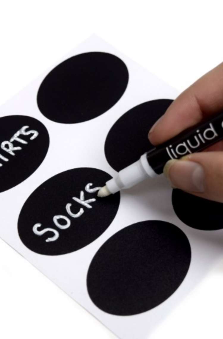 Chalkboard labels with a hand holding liquid chalk pen writing "socks" one of the the labels. Label above says "shirts"