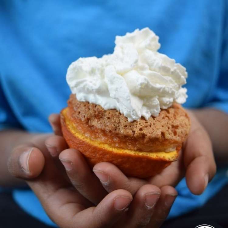 Orange Peel Uses - Someone holding a cupcake topped with whipping cream and nestled in orange peel as cupcake liner