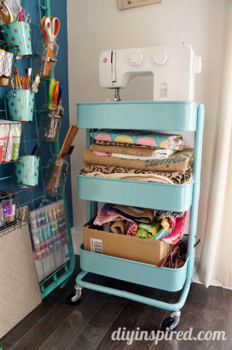 blue rolling cart with a sewing machine on the top shelf and fabric on the other shelves in a sewing room