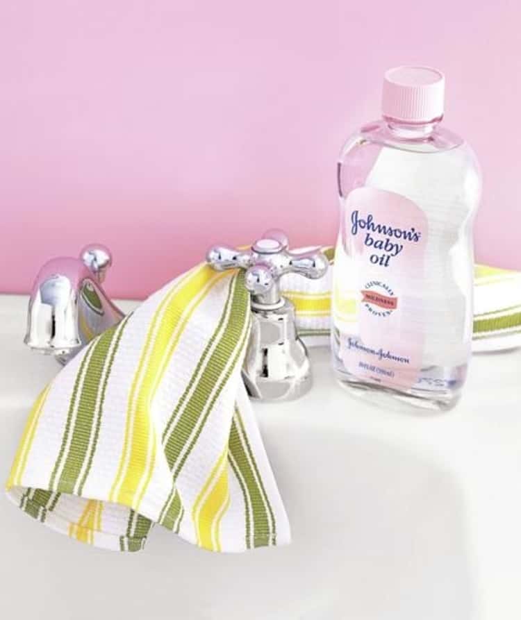 bottle of baby oil on bathroom sink next to shiny polished taps and cotton cloth