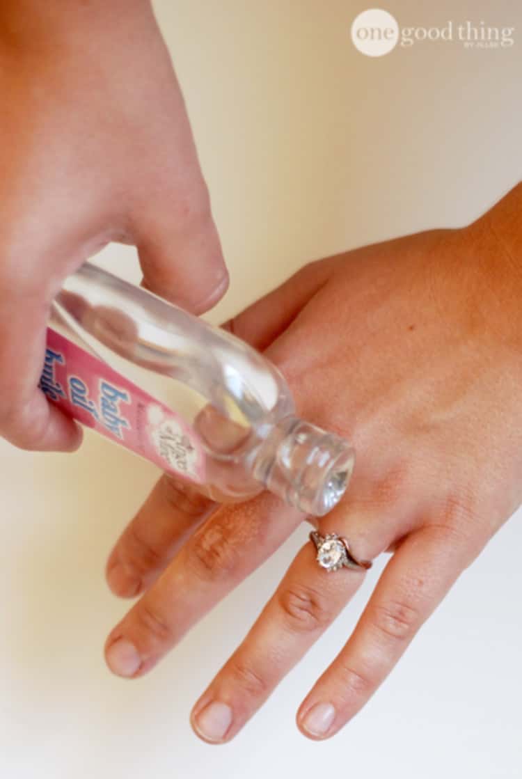 baby oil uses - person's right hand pouring baby oil on person's left hand ring finger
