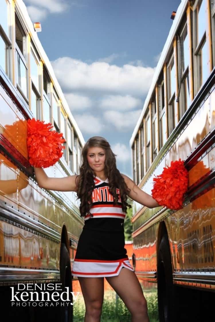 senior picture ideas for girls - cheerleader holding pompoms in her hands while standing between 2 buses