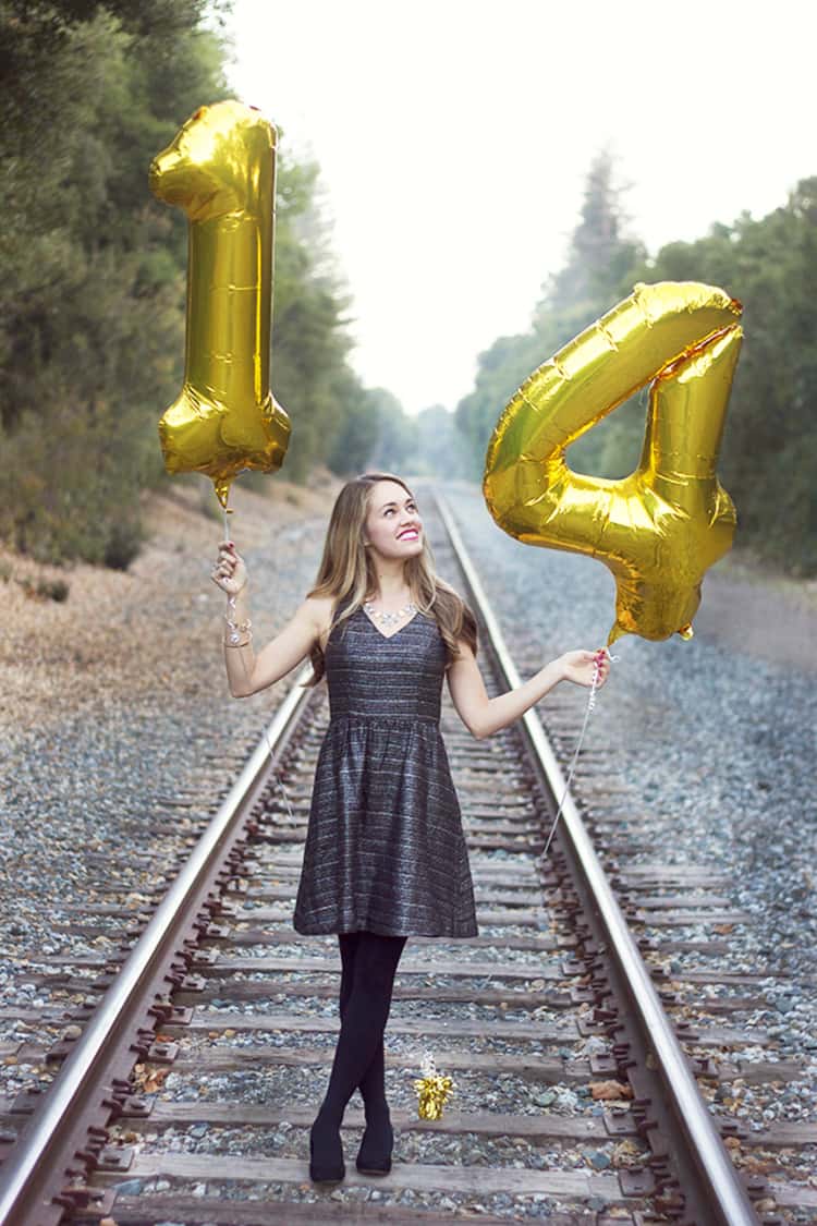 senior picture ideas for girls - girl standing on railtrack holding up 2 number-shaped balloons in her hands