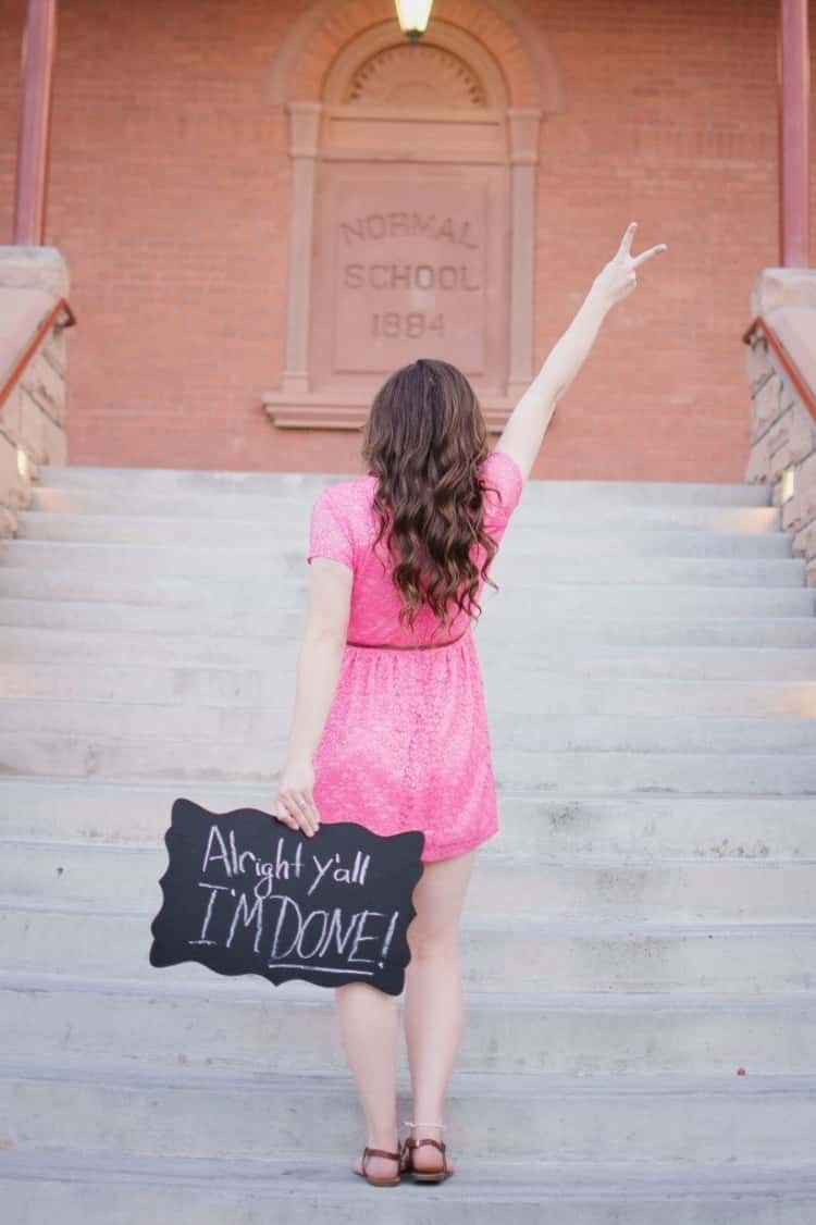 senior picture ideas for girls - girl in pink dress facing away from camera and holding chalkboard sign behind her in left hand written 'Alright y'all, I'M DONE!' while her right hand is held up in a victory sign