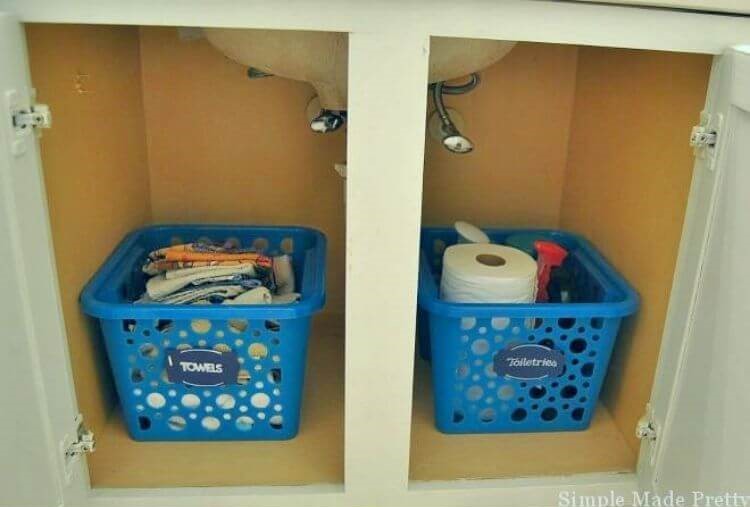 baskets with labels filled with toiletry items like toilet paper and wash clothes to organize under the bathroom sink