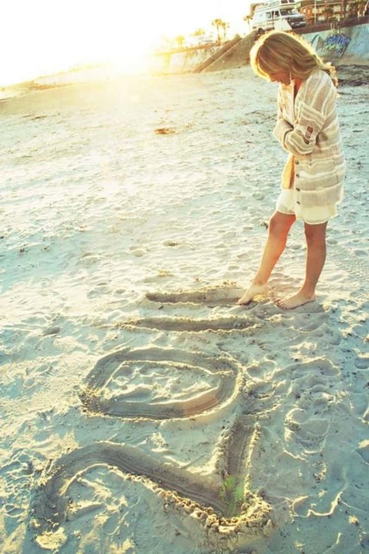 senior picture ideas for girls - girl on beach writing in the sand with her toes