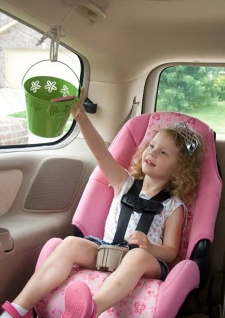 Travel hack little girl in car seat using a pulley system to move a bucket from front to back of car easily