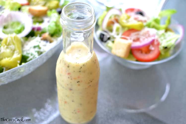 Italian Dressing in a glass bottle next to two salads
