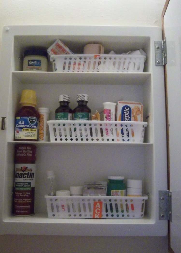 medicine cabinet organized with small white plastic baskets