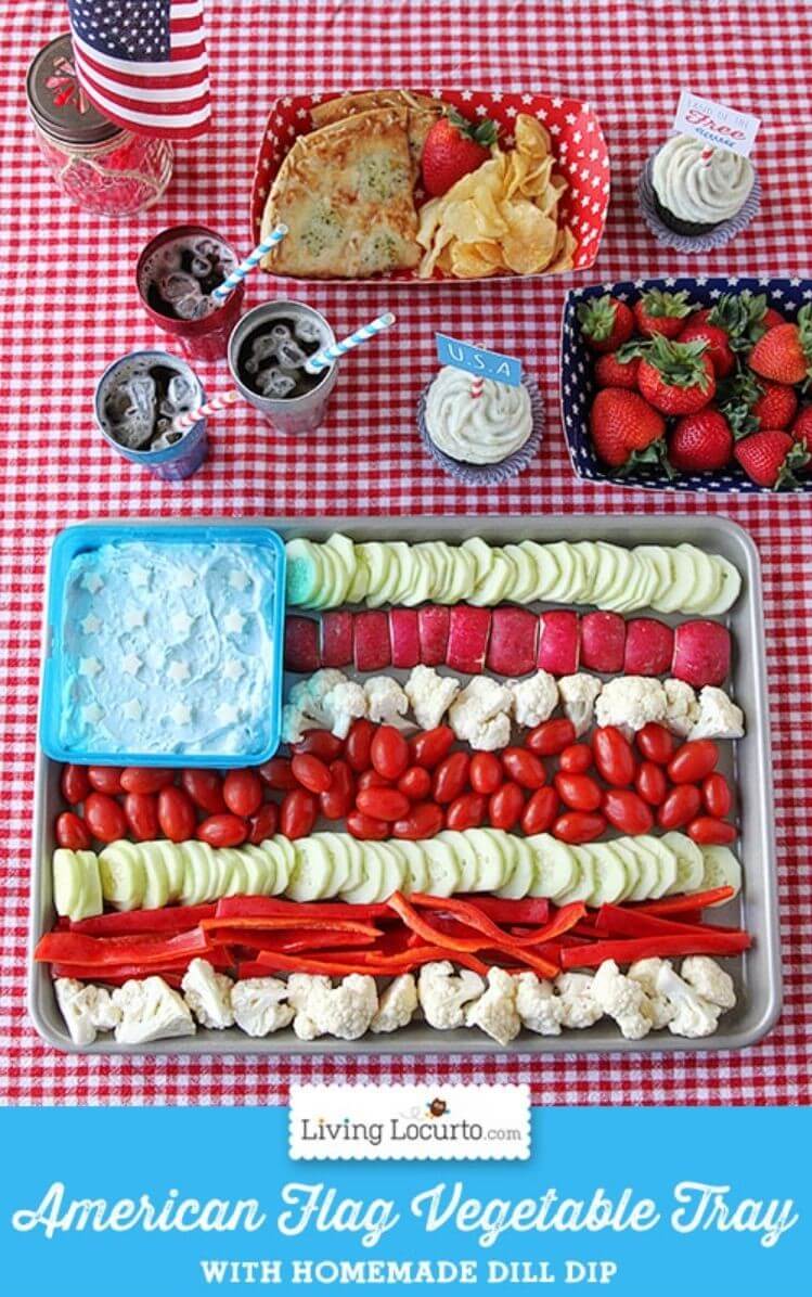 A table with a veggie tray shaped like an American flag, drinks, strawberries, and veggie dip for a 4th of July BBQ