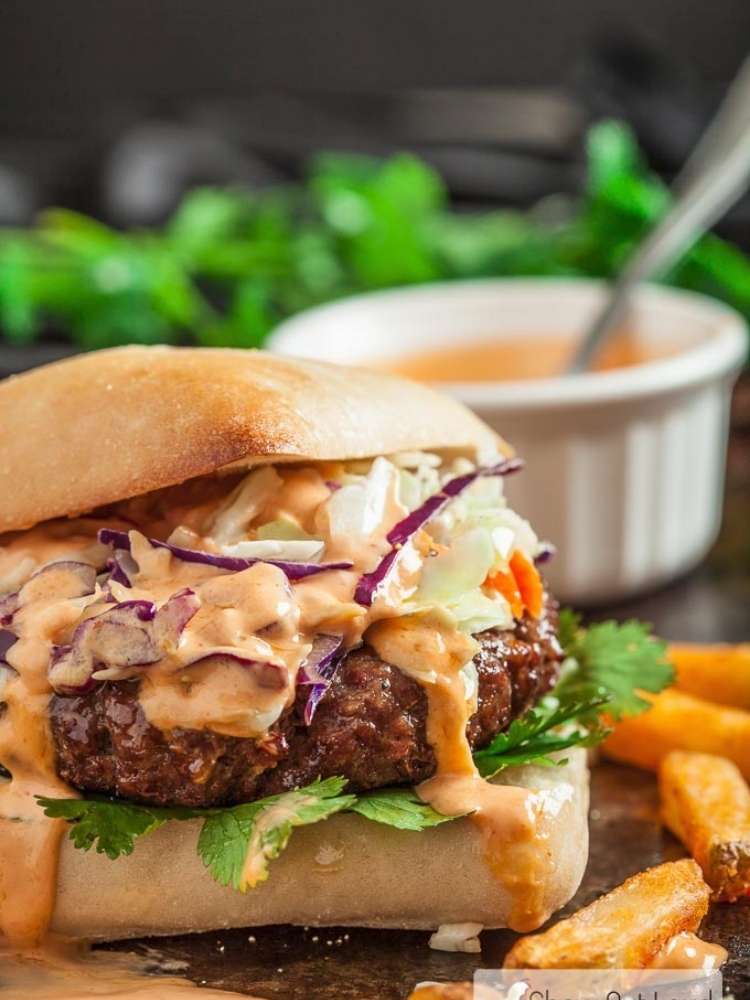 A beef burger with cilantro, sriracha mayo, and cole slaw.