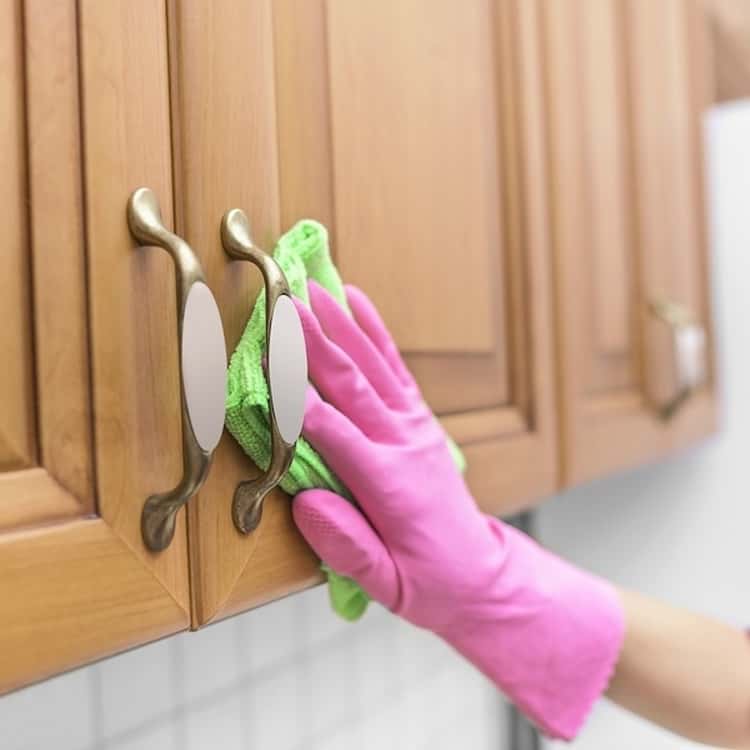 cleaning wood cabinets - gloved hand wiping wood cabinets with rag