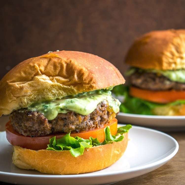 beef burger topped with tomato, lettuce, and a avocado sauce.