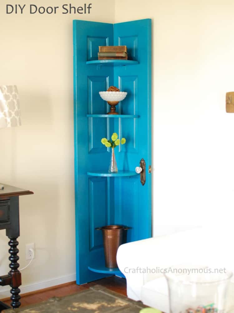 old door painted blue and turned into a corner shelf with things on the shelfs like a vase, books, and flowers