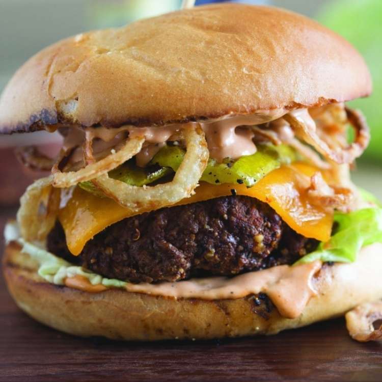 Beef burger on a bun topped with fried onion straws, cheddar cheese, lettuce and a barbecue mayonnaise.