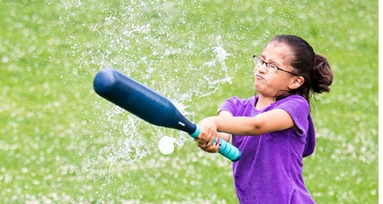 Girl hitting water balloon with baseball bat