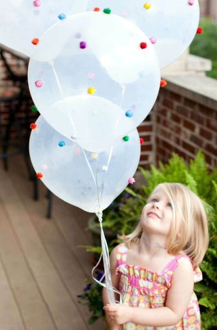 OneCrazyHouse Party Food Ideas small girl looking up at two balloons she is holding with fabric pom poms flued to the floating balloons